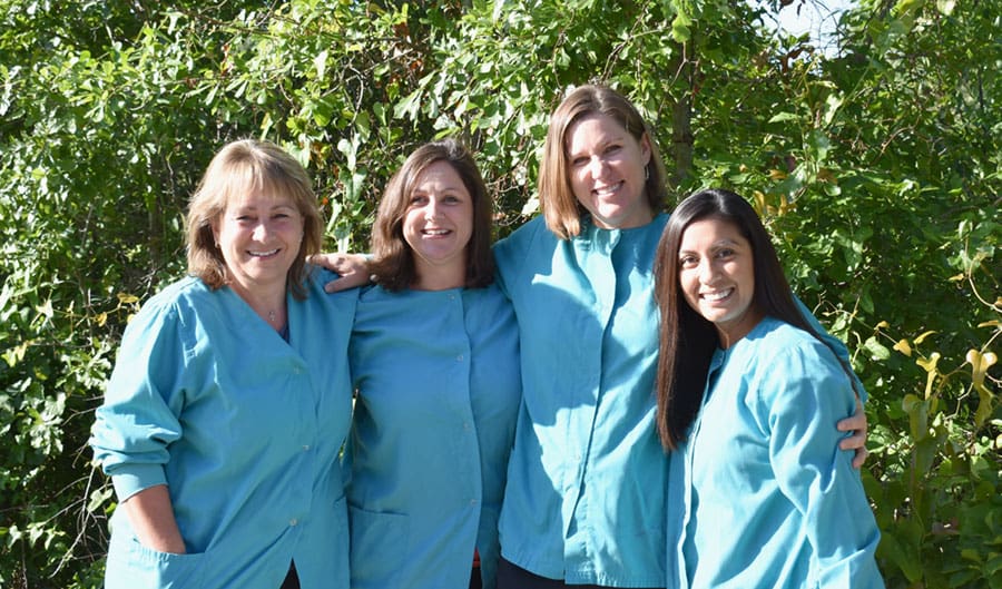 A group of four dental assistants in light blue scrubs