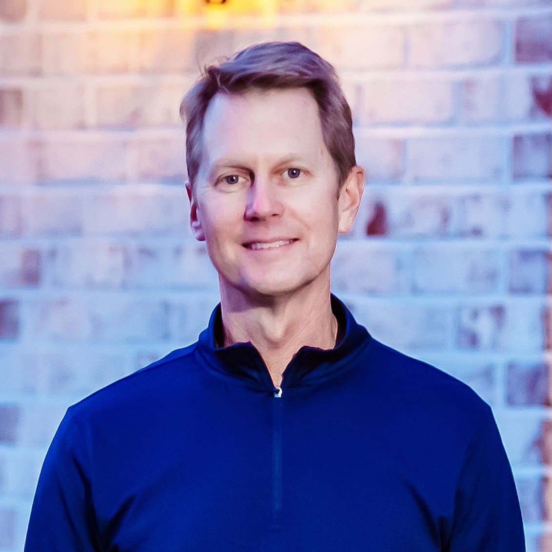 Dr. Mark Castor smiling in a blue dress shirt standing in front of a palm tree